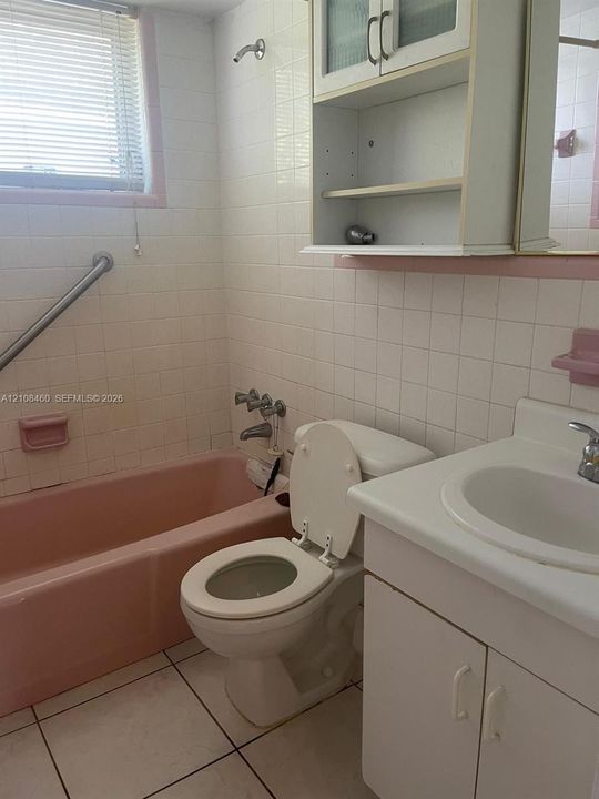 Bathroom featuring a porcelain bathtub, white tile wall surround, built-in medicine cabinet with shelving, vanity with a white countertop, and tiled flooring