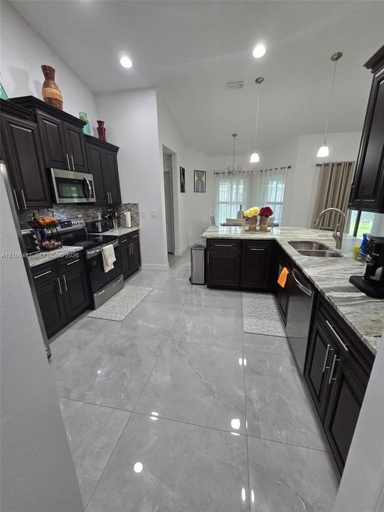 Kitchen featuring dark wood cabinetry, large-format polished tile flooring, stone-finish countertops, stainless steel appliances, and pendant lighting