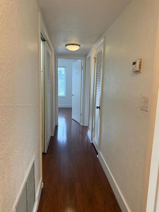 Hallway featuring wood-finish flooring, two sets of louvered closet doors, and a flush-mount ceiling light fixture