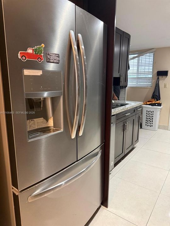 Stainless steel French door refrigerator with exterior water and ice dispenser, dark-toned cabinetry, light-toned stone-finish countertops, and tile flooring