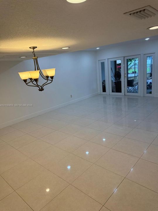 Large-format tile flooring, recessed ceiling lighting, and a multi-arm chandelier with glass shades, featuring double glass-paneled exterior doors with flanking sidelights