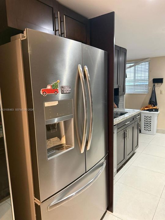 Stainless steel French-door refrigerator, dark-finish cabinetry with silver-tone hardware, stone-composite countertops, and tile flooring