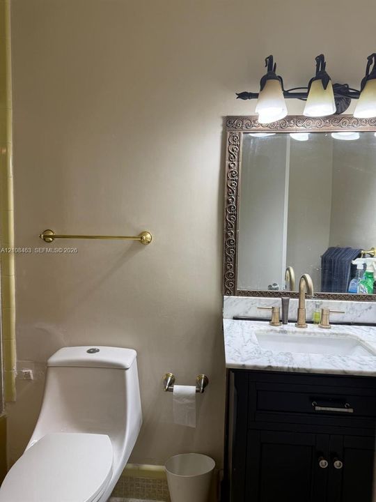 Bathroom vanity featuring a dark-finish base, stone countertop with integrated basin, three-light fixture, decorative framed mirror, and metallic hardware accents