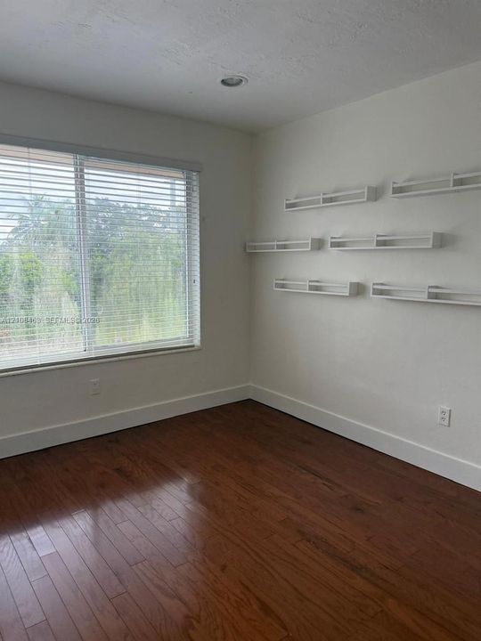 Room featuring wood-finish flooring, a large window with horizontal blinds, and multiple built-in wall-mounted shelves