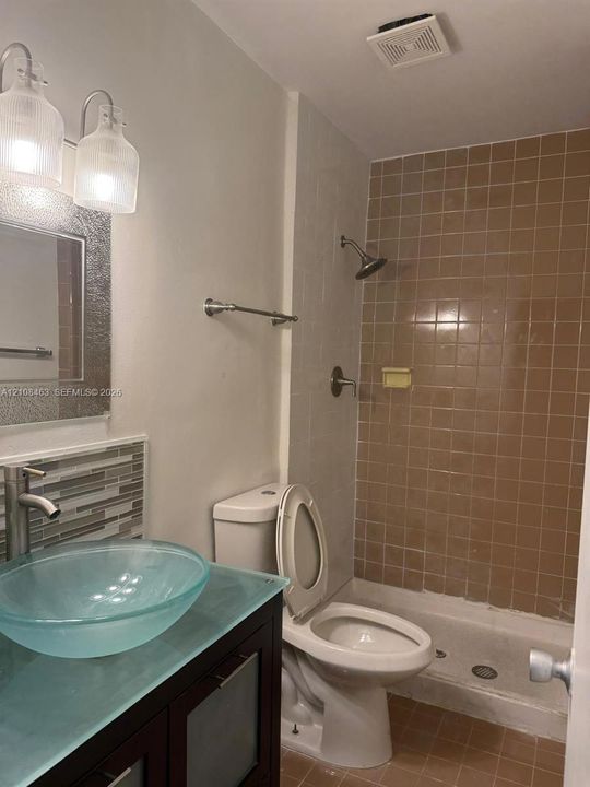 Bathroom featuring a dark wood-finish vanity, glass vessel sink, mosaic tile backsplash, and a tub-shower combination with ceramic wall tile