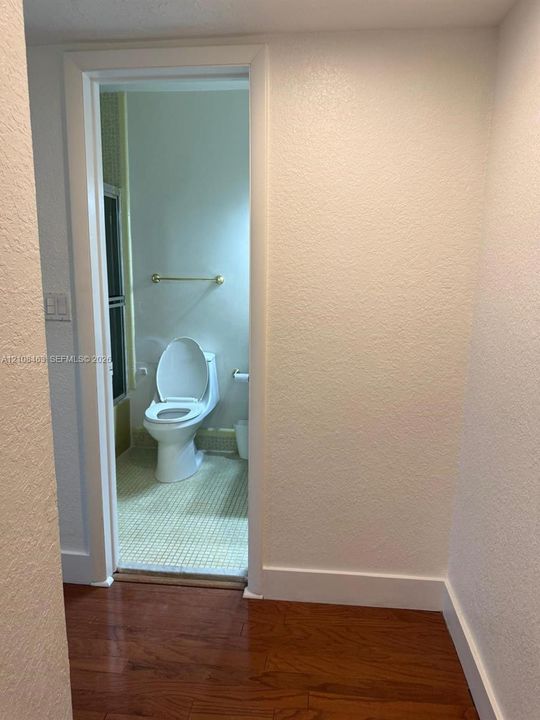 Bathroom featuring a white ceramic toilet, gold-toned towel bar, and tiled flooring, framed by wood-finish flooring in the exterior space