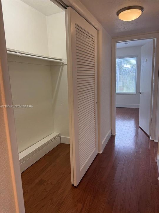Closet featuring louvered sliding doors, wood-finish flooring, and a built-in hanging rod, illuminated by a flush-mount ceiling fixture