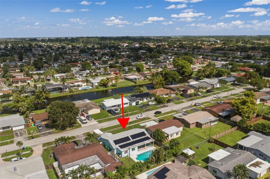 Aerial perspective of property featuring a roof-mounted solar panel system, private swimming pool, concrete driveway, and grass lawn