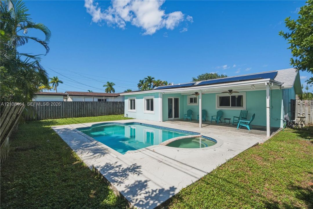 Backyard featuring a concrete pool deck, integrated in-ground pool and spa, covered patio area, and perimeter privacy fencing