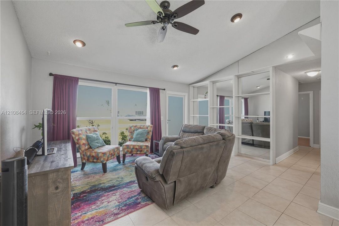 Vaulted ceilings featuring recessed lighting, a multi-blade ceiling fan, large windows, and a floor-to-ceiling mirror-paneled partition