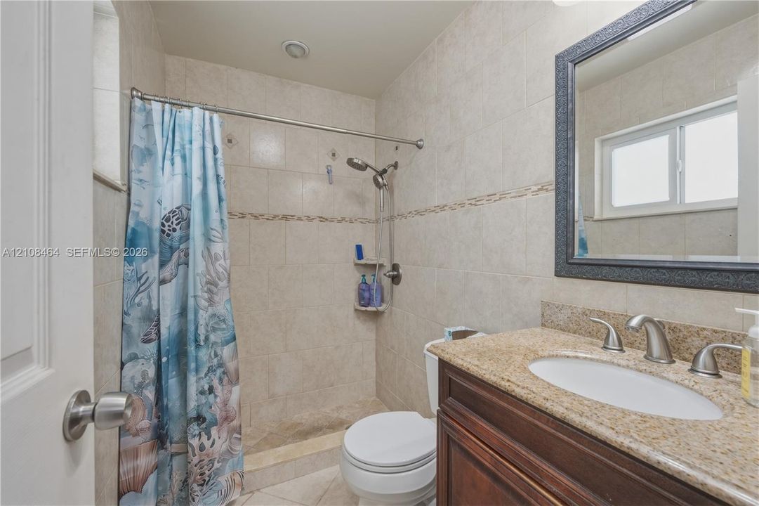 Full-height tiled shower surround with built-in corner shelving, stone-composite vanity countertop, integrated sink with dual-handle faucet, and framed wall-mounted mirror