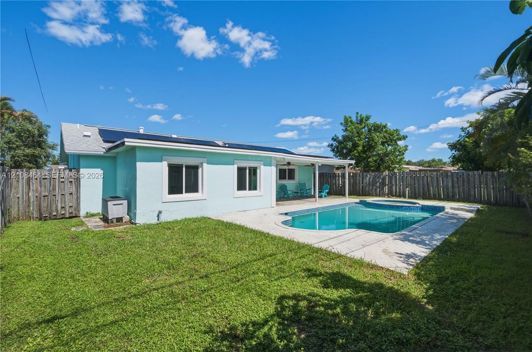 Backyard featuring a concrete-decked swimming pool with integrated spa, covered patio, solar panels, and wood privacy fencing