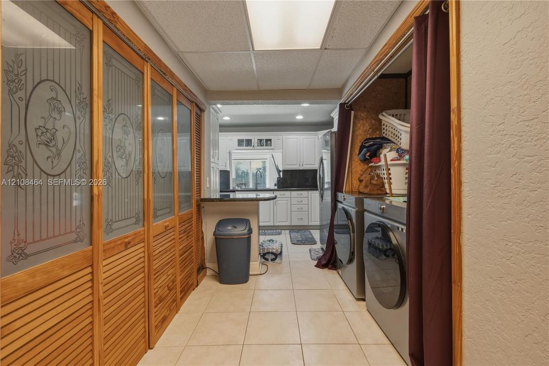 Laundry area featuring natural wood louvered doors with decorative glass panel inserts and neutral tile flooring
