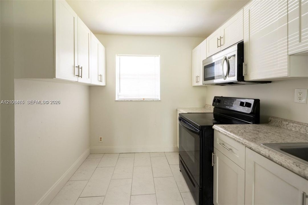 Kitchen featuring white cabinetry, stone-finish countertops, black appliances including a range and over-the-range microwave, and tile flooring