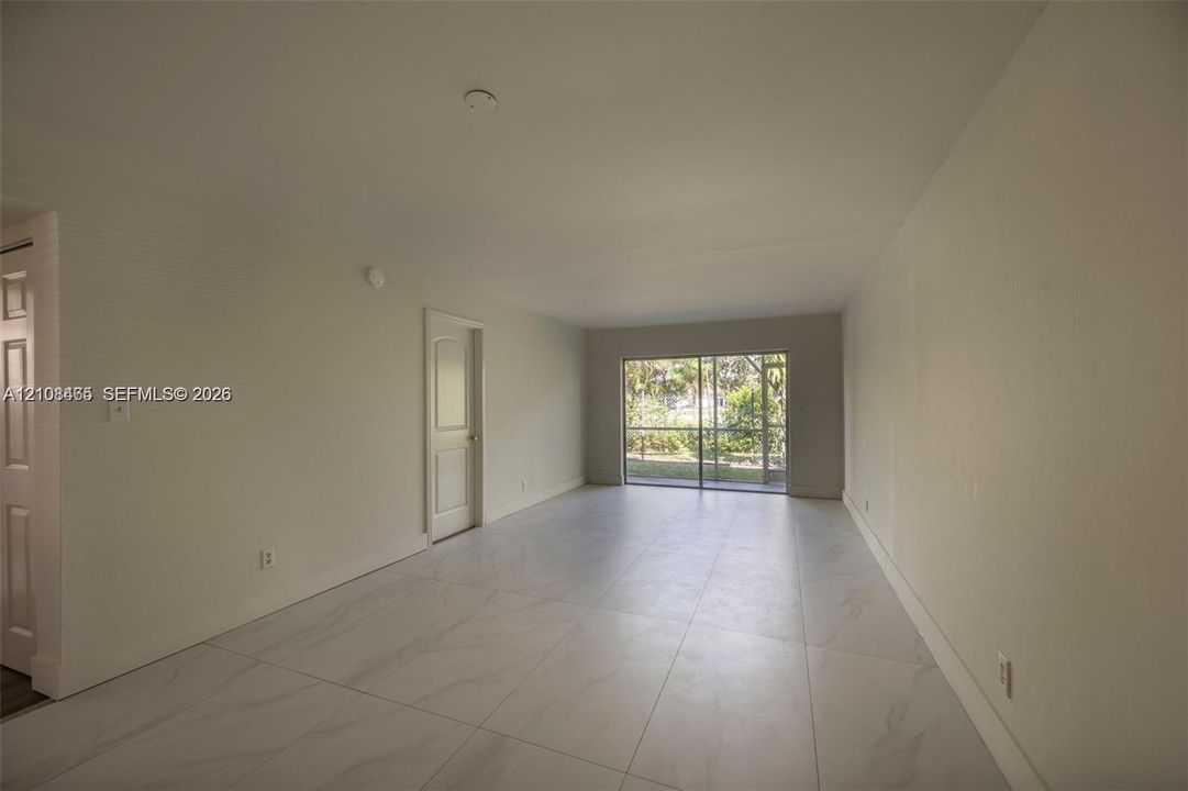 Large-format tile flooring, neutral walls, and a multi-panel sliding glass door leading to a screened enclosure