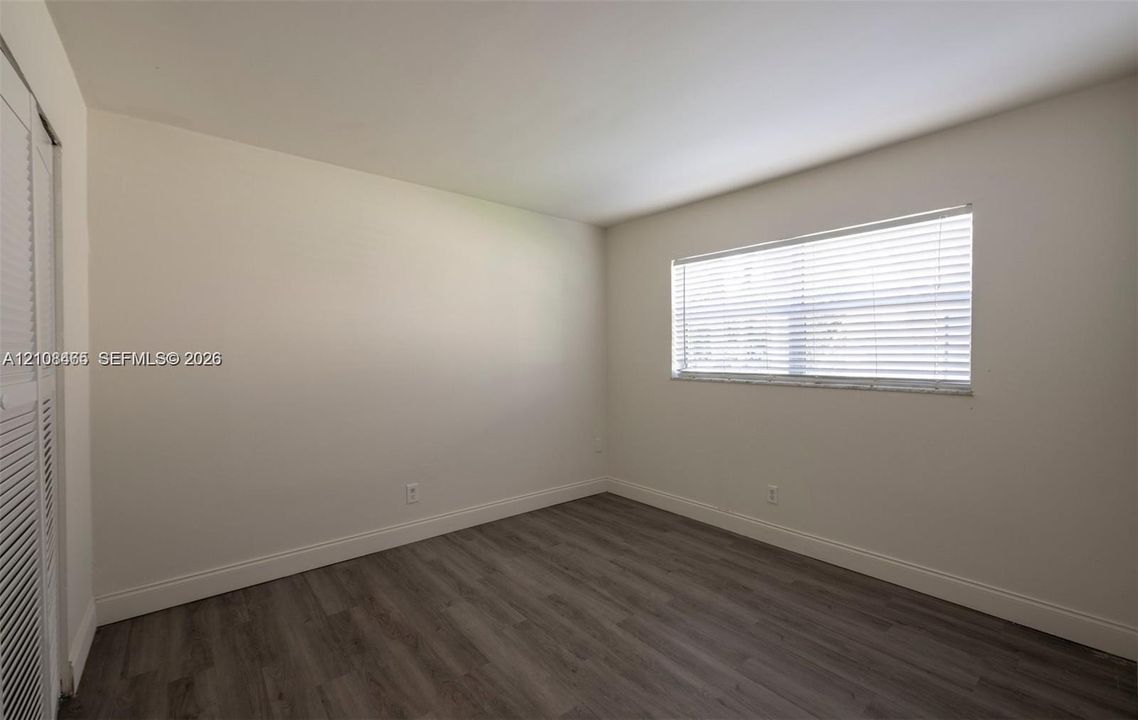 Interior space featuring neutral wall paint, wood-finish flooring, a window with horizontal blinds, and louvered closet doors