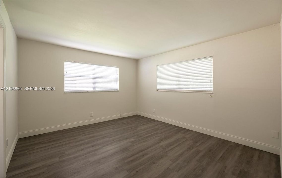 Neutral-toned walls and wood-finish flooring featuring two horizontal windows with fitted horizontal blinds