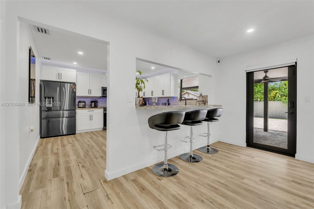 Kitchen featuring white shaker cabinetry, stone-finish countertops, stainless steel appliances, wood-finish flooring, and a breakfast bar cutout