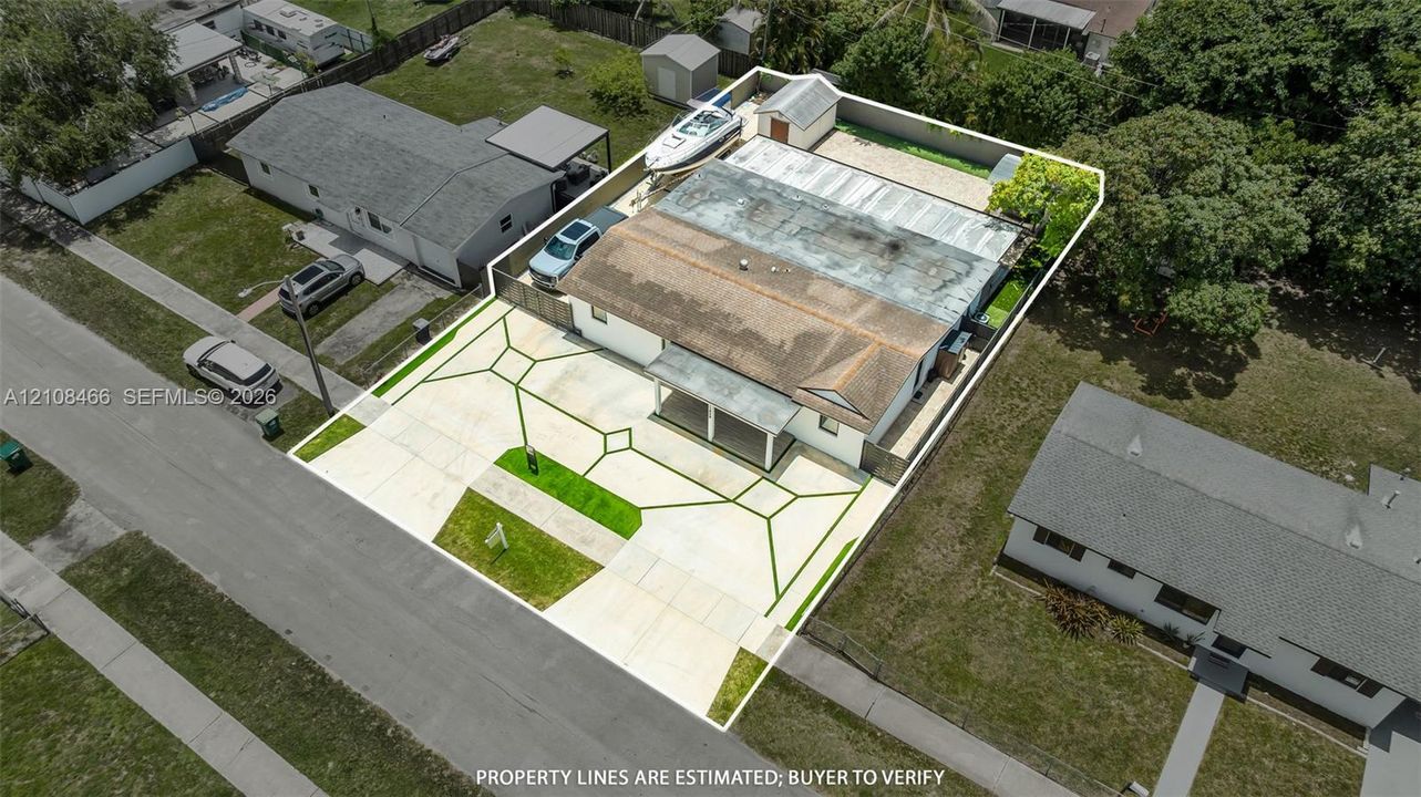 Aerial perspective of property featuring a wide concrete driveway, covered front entryway, fenced perimeter, and detached storage structure
