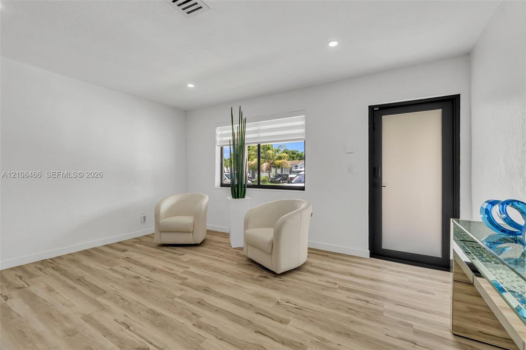 Interior space featuring wood-finish flooring, recessed lighting, a window with horizontal blinds, and a door with a frosted glass panel and black trim