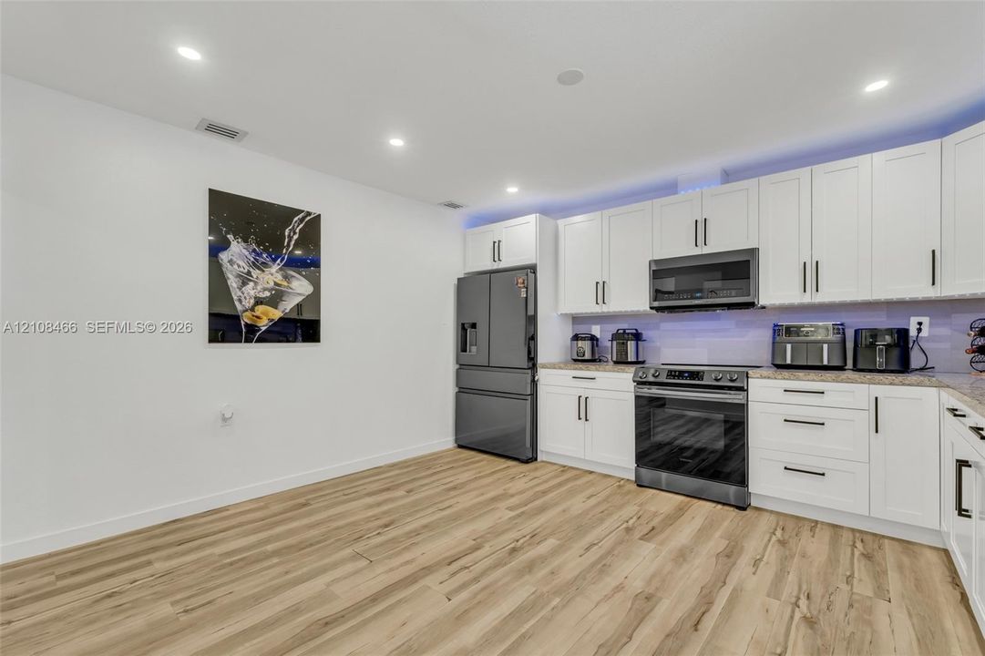 Kitchen featuring shaker-style white cabinetry, wood-finish flooring, recessed lighting, and stainless-steel appliances