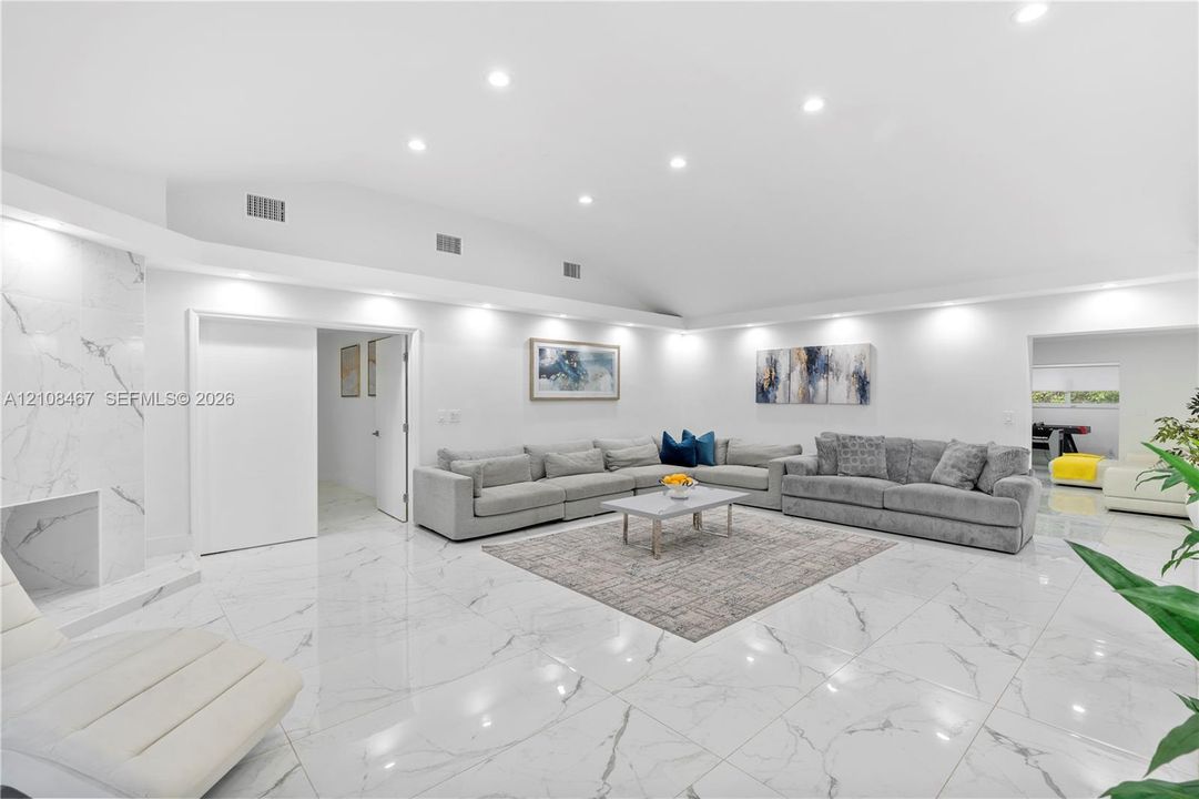 Open-concept interior featuring high vaulted ceilings, large-format tile flooring with a neutral finish, and a floor-to-ceiling stone-surround fireplace