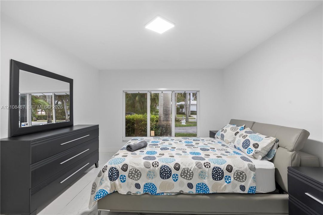 Neutral-toned interior space featuring white walls, bright flush-mount ceiling lighting, large horizontal window, and wood-finish flooring