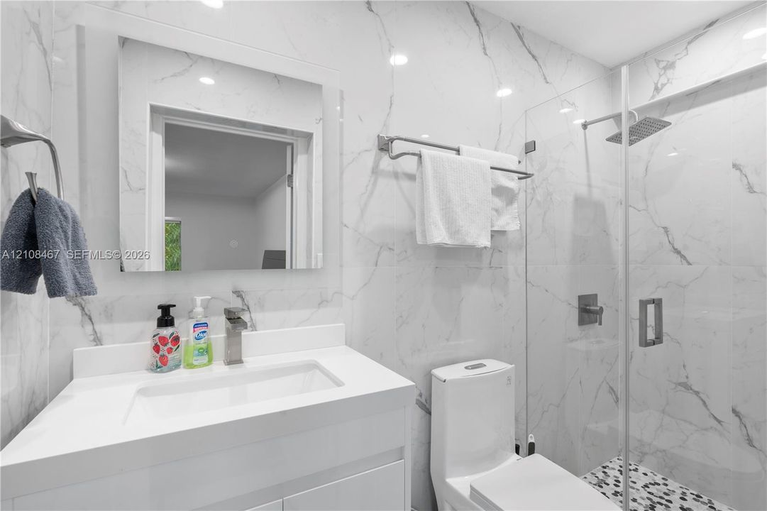 Bathroom featuring large-format wall tiling with veining detail, glass-enclosed shower with a rainfall showerhead, vanity with integrated basin, and modern polished metal fixtures