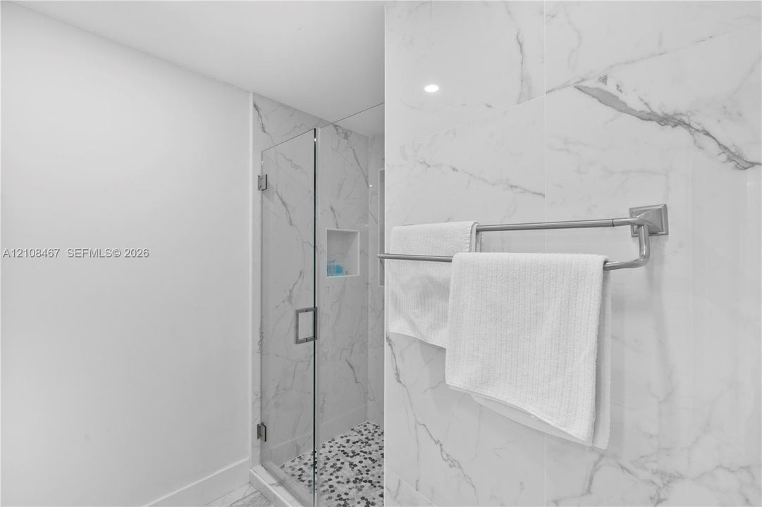 Shower featuring large-format veined wall tile, glass enclosure, built-in wall niche, and pebble-finish floor tile