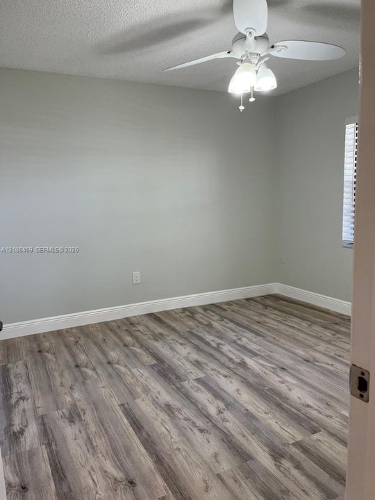 Wood-finish flooring, neutral wall tones, white ceiling fan with integrated three-light fixture, and window blinds