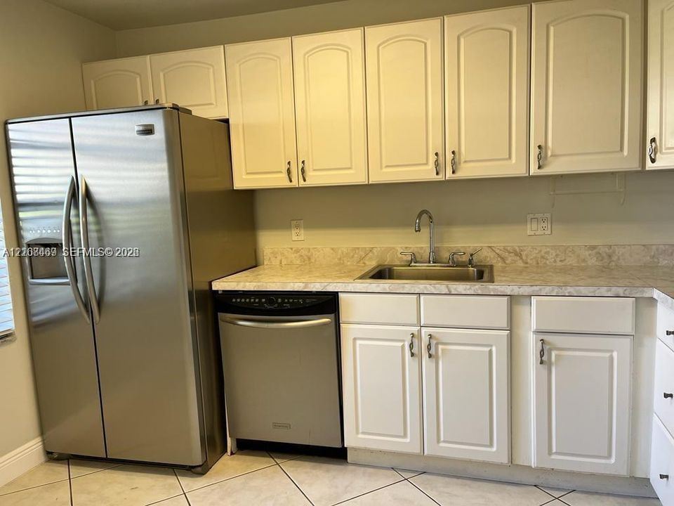 Kitchen featuring white shaker-style cabinetry, neutral patterned countertops, stainless steel appliances which includes side-by-side refrigerator, dishwasher, electric range and microwave-hood