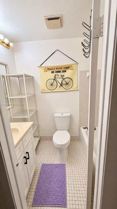 Bathroom featuring a white vanity cabinet with a light-toned countertop, a multi-tier white metal shelving unit, a white porcelain toilet, and a bathtub with white square tile surround