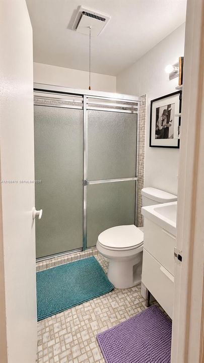 Shower featuring a sliding glass enclosure with metal frame, mosaic-tiled accent wall, vanity with integrated basin, and patterned tile flooring