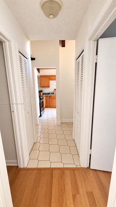 Hallway featuring wood-finish flooring, dual louvered-style closet doors, geometric tile flooring, and a flush-mount ceiling fixture