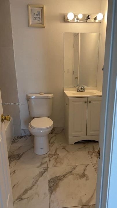 Bathroom featuring large-format tile flooring with a neutral-toned veined pattern, a white vanity with integrated basin, polished chrome hardware, and a three-light vanity fixture
