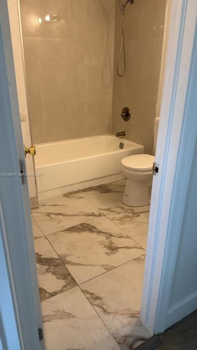 Bathroom featuring large-format tile flooring with a neutral veined pattern, a porcelain bathtub, and wall-mounted shower hardware in a metallic finish