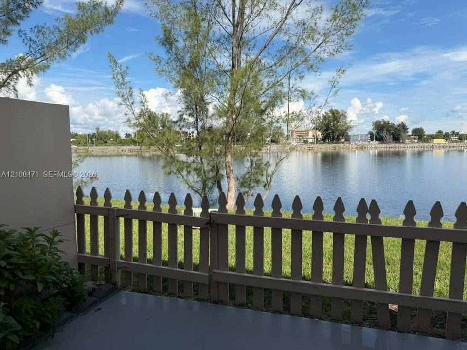 Concrete patio featuring a picket fence, manicured lawn, and water frontage