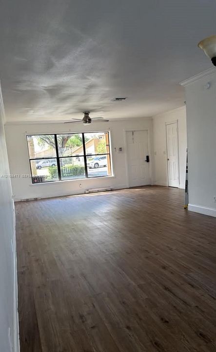 Open-concept interior featuring wood-finish flooring, a large picture window, a ceiling fan, and crown molding