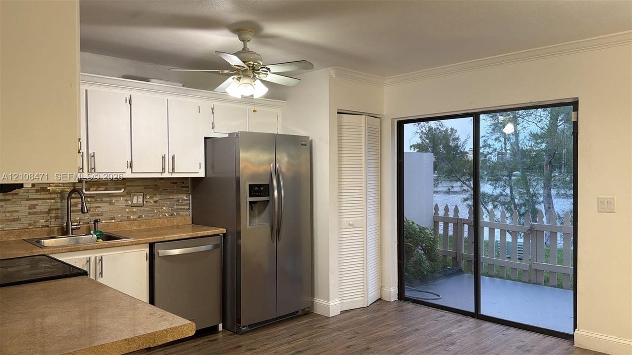 Kitchen featuring white cabinetry, stainless steel appliances, multi-toned stone-tile backsplash, wood-finish flooring, and sliding glass doors with access to an exterior patio