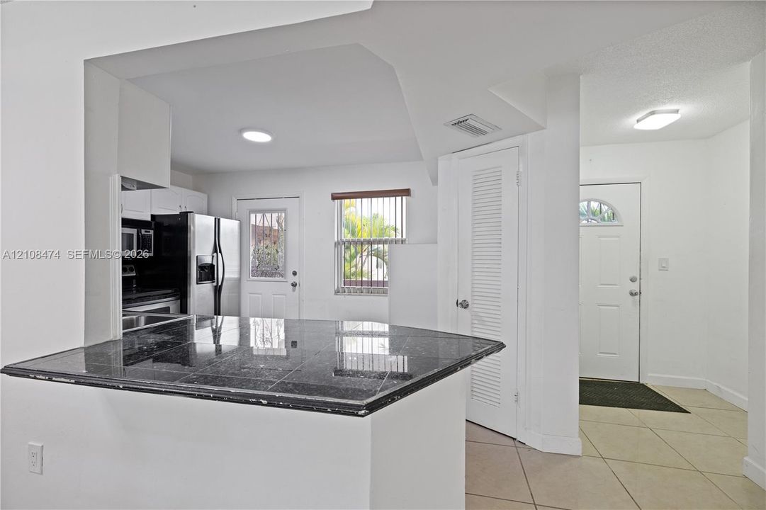 Kitchen featuring stone-surfaced breakfast bar, stainless steel appliances, neutral tile flooring, and flush-mount ceiling lighting