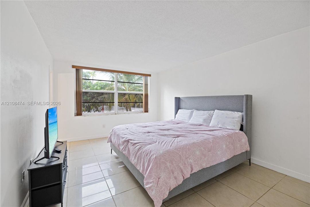 Neutral-toned interior space featuring light-colored large-format tile flooring, expansive window with horizontal blind hardware, and crisp white wall finishes