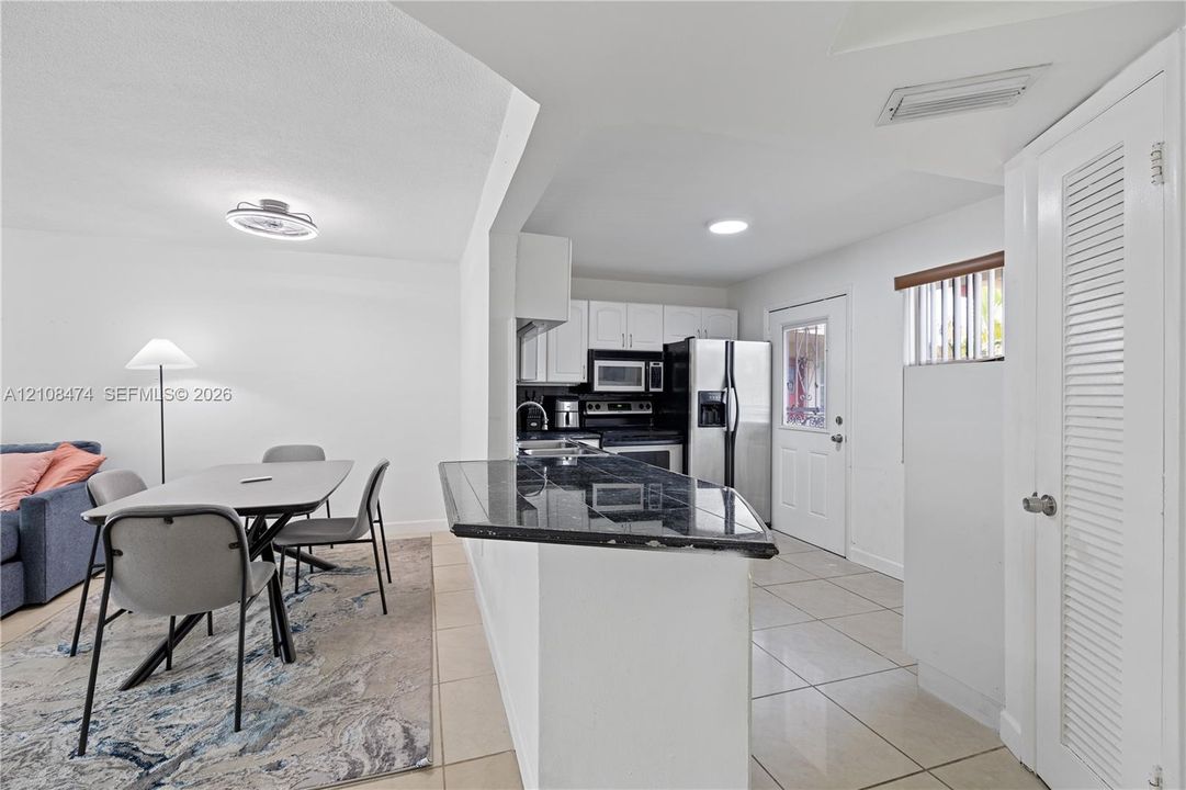 Kitchen featuring dark stone-surfaced breakfast bar, white cabinetry, integrated stainless steel appliances, and neutral tile flooring throughout