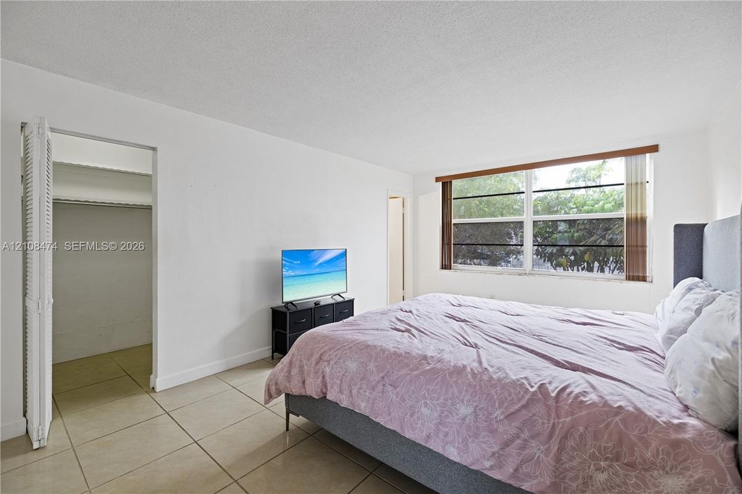 Neutral-toned tile flooring, large multi-pane window with wood-finish trim, and walk-in closet with bi-fold door