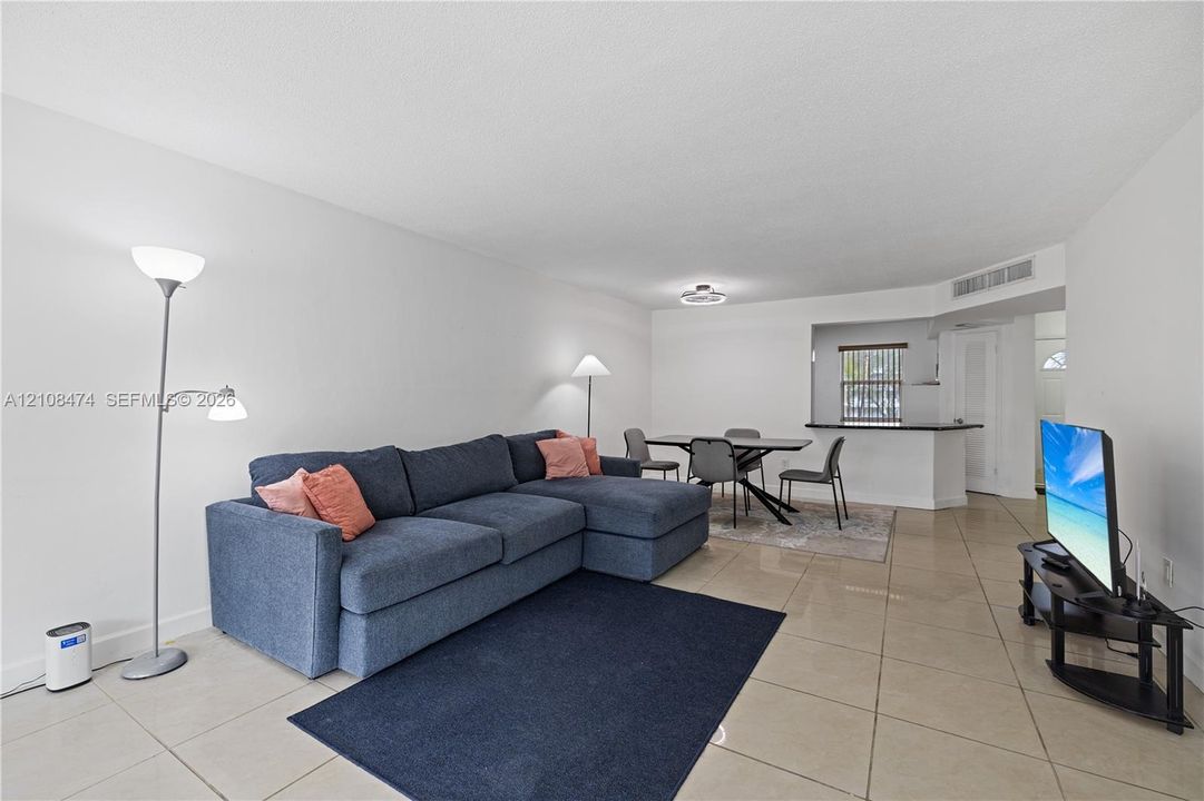 Open-concept interior featuring oversized tile flooring, a kitchen pass-through window with a breakfast bar, and recessed lighting