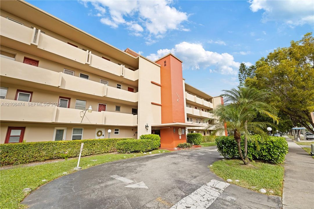 Multi-story exterior featuring a stucco facade, accent orange pillar, private recessed balconies, and manicured landscaping
