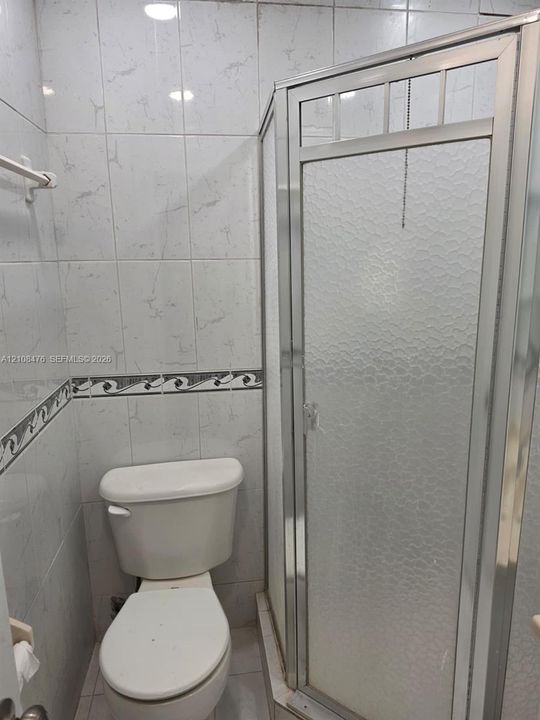 Bathroom featuring floor-to-ceiling ceramic tile, decorative accent trim, a corner shower enclosure with textured glass panels, and a standard-height toilet