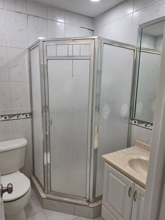 Corner shower stall with a metal-framed glass enclosure, vanity with a molded countertop and basin, ceramic tile wall finishes with decorative accents, and polished edge mirror