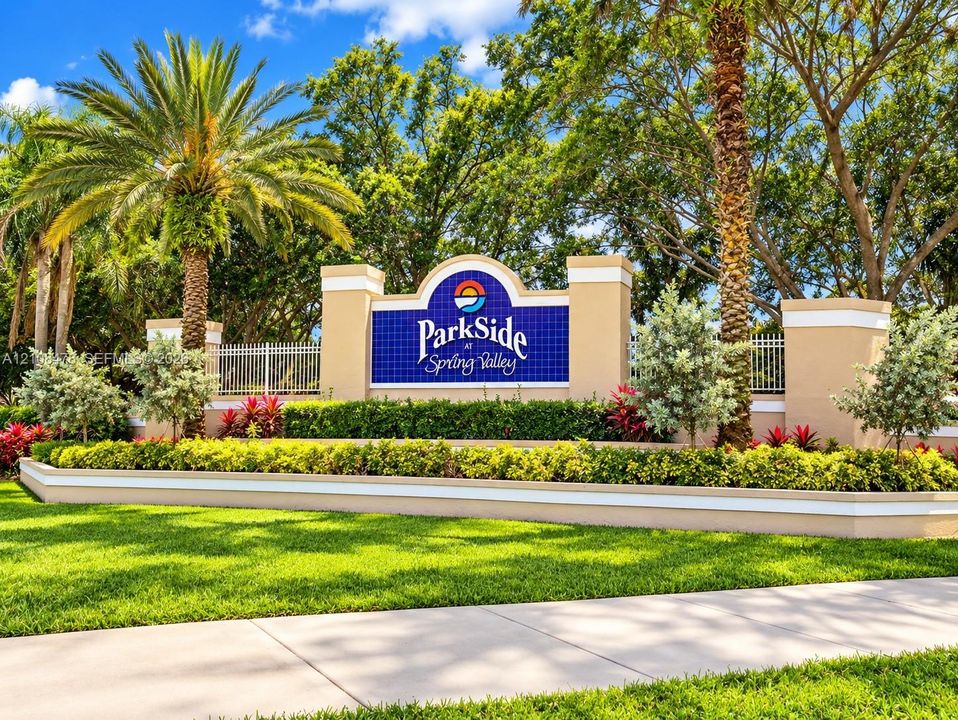 Community entrance signage featuring masonry pillar accents, manicured landscaping, mature palm trees, and decorative metal fencing
