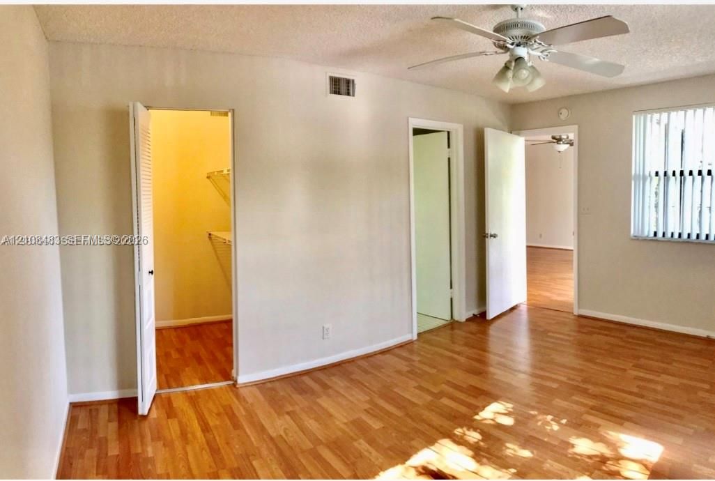 Wood-finish flooring, ceiling fan with integrated light fixture, walk-in closet with built-in wire shelving, and window with vertical blinds