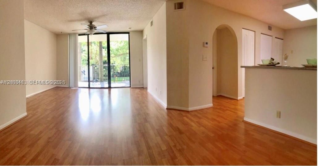 Open-concept living space featuring wood-finish flooring, sliding glass doors, a ceiling fan, and a prominent arched entryway